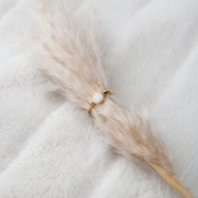 Bague perle dorée au lait maternel posée sur une plume de pampa